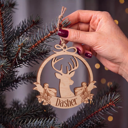 Hand places laser cut plywood reindeer ornament with engraved Dasher ribbon onto pine branches with warm lights.