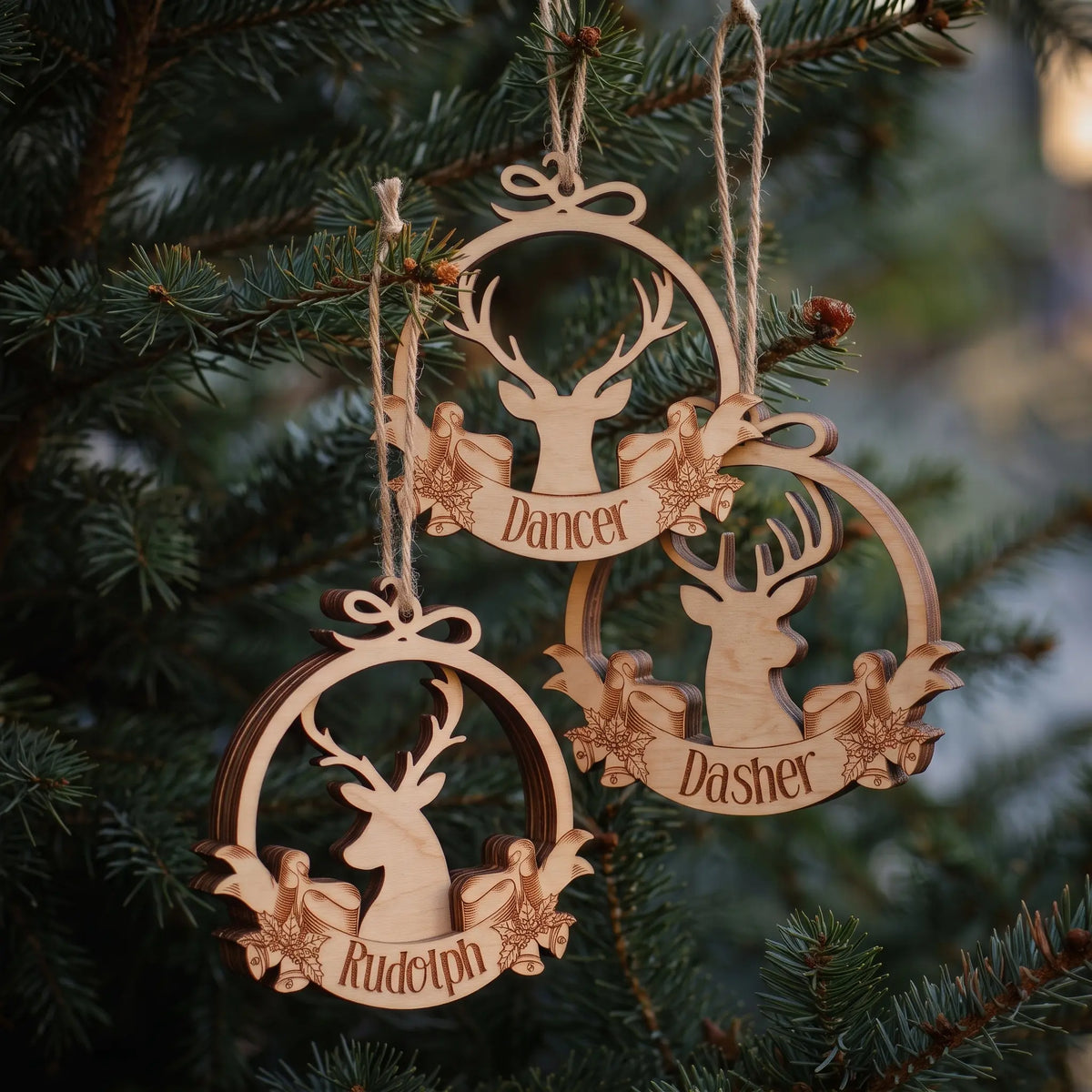 Three laser cut plywood reindeer baubles with engraved names Rudolph, Dancer, and Dasher hanging together on a tree.
