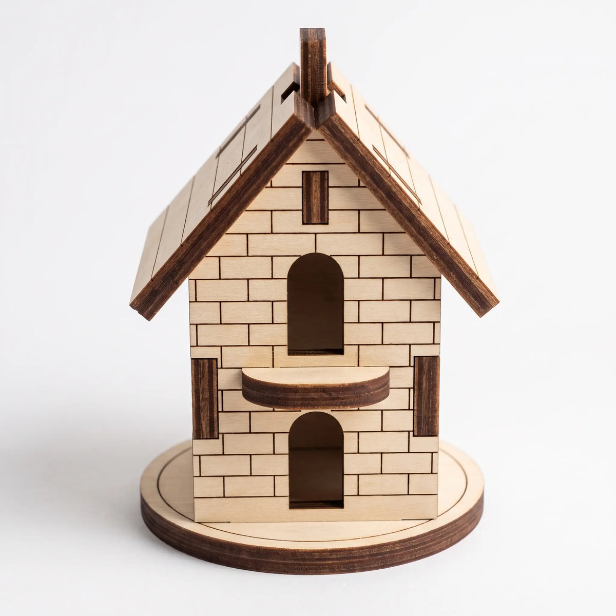 Front view of 3D laser cut plywood Christmas house figurine on circular base with small balcony over plain white background.