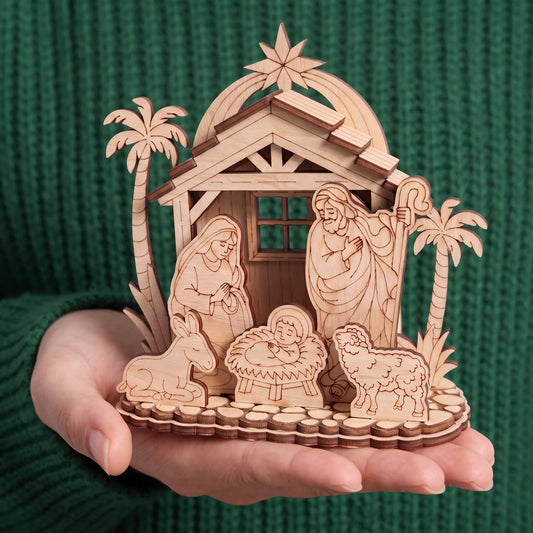 Hand holds assembled laser cut plywood nativity set with holy family and palms, showing scale against green sweater