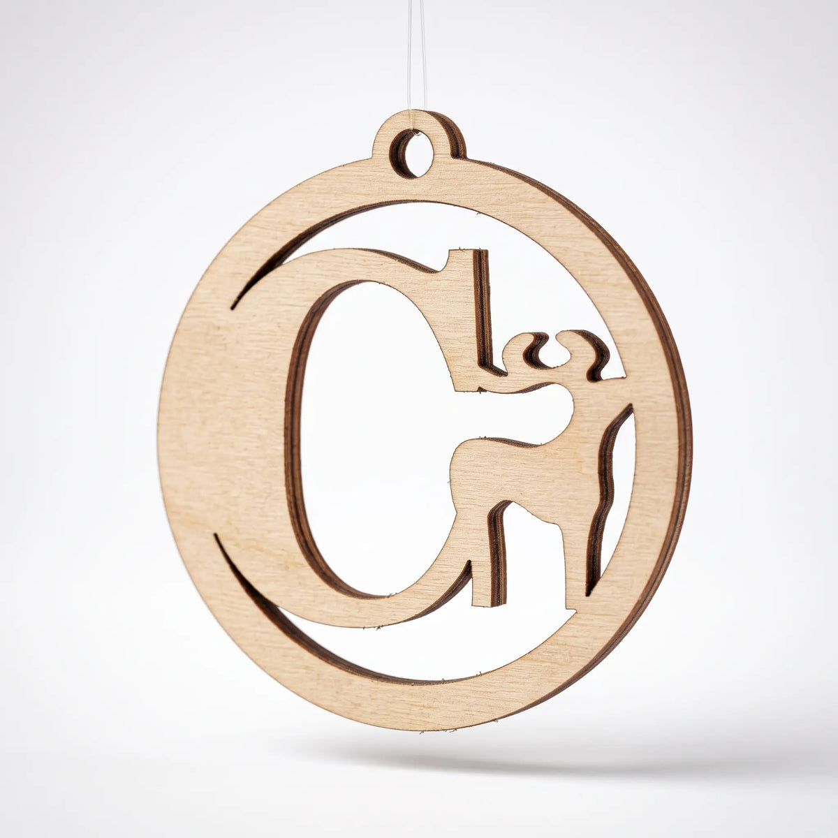 Laser cut plywood round monogram bauble with letter C and deer silhouette suspended against plain white backdrop. (
