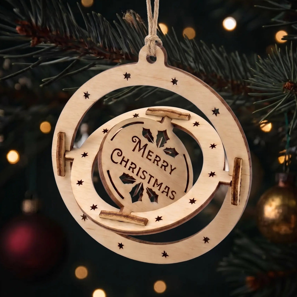Kinetic laser cut plywood rotating sphere ornament with engraved Merry Christmas disc on glowing holiday tree