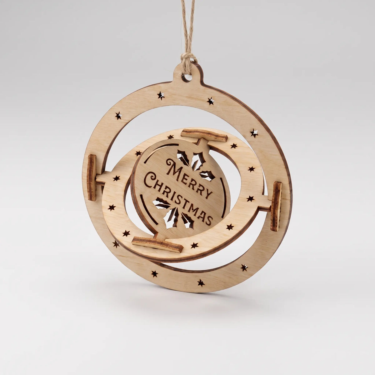Laser cut plywood 3D kinetic spinning bauble with Merry Christmas center disc hanging isolated on white backdrop