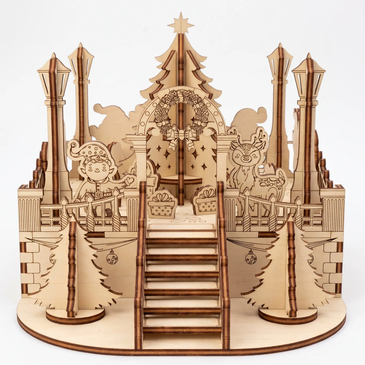 Front view of laser cut plywood holiday town square diorama with staircase, central tree, elf, and deer on white.