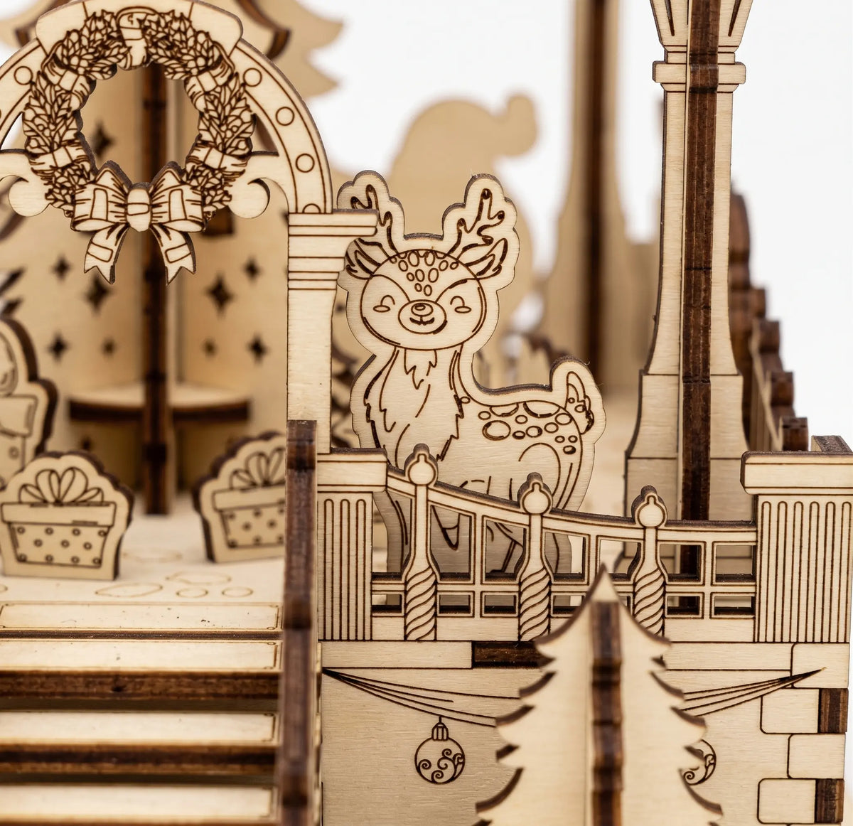 Macro view of laser cut plywood holiday town square diorama highlighting engraved deer figure, wreath, and railings