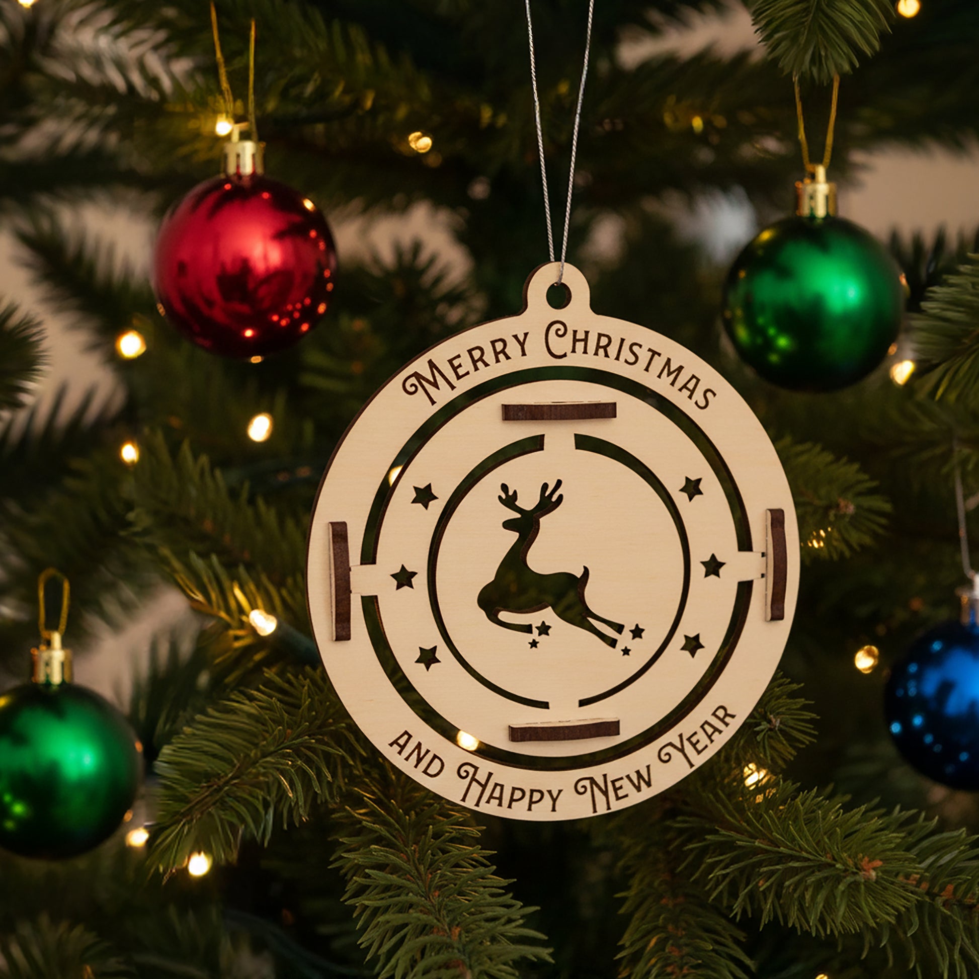 Intricate laser cut Christmas tree toy deer with a rotating leaping deer and star details on a hanging circle ornament, set against a warm twinkling Christmas tree background.