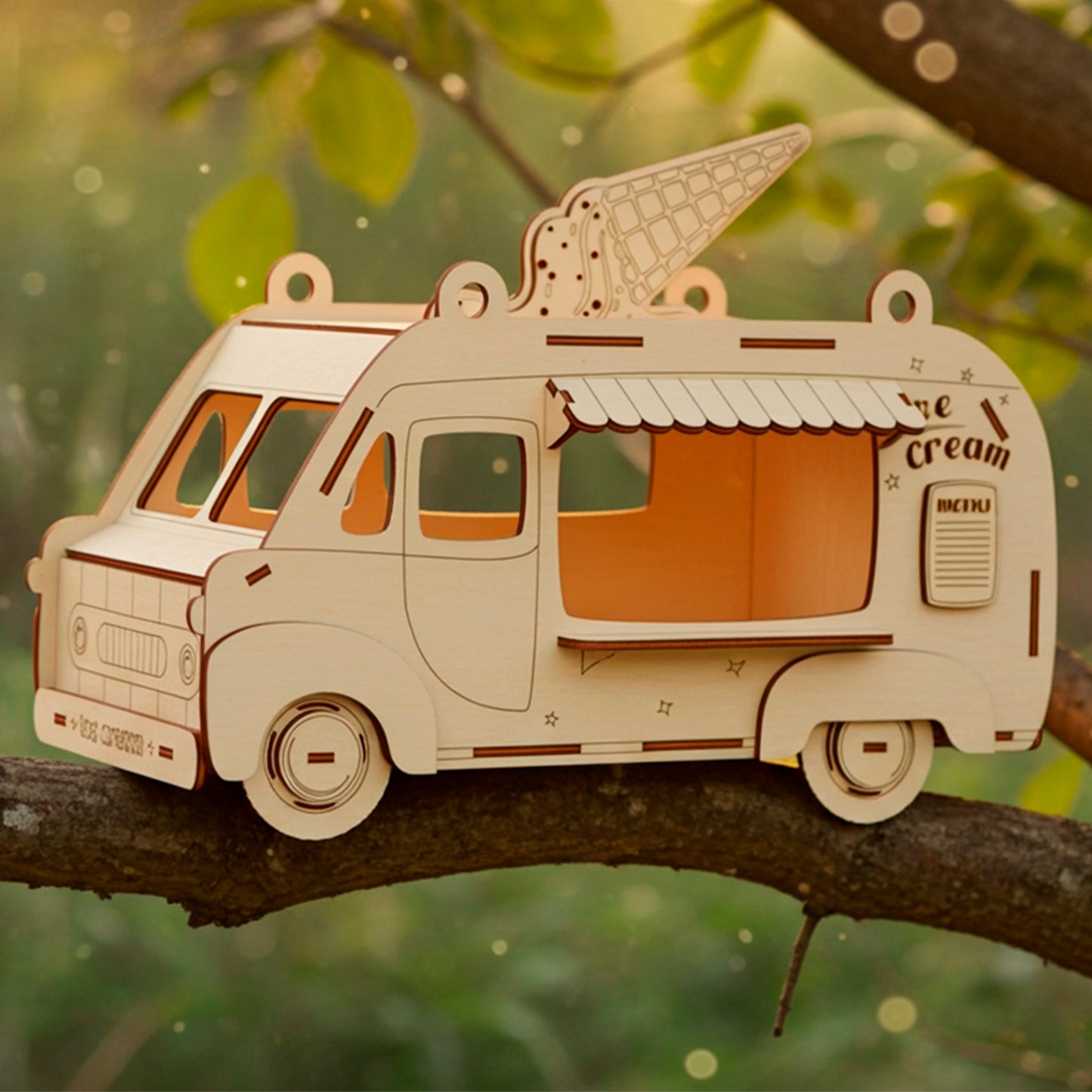 Laser cut wooden plywood Ice Cream Van Birdhouse or treat dispenser, shown lying on a green tree branch in a natural outdoor setting with warm golden hour sunlight. The model features an engraved ice cream cone on the roof, a menu sign, and wheels, showcasing the detailed DIY craft kit or ready-made whimsical gift.