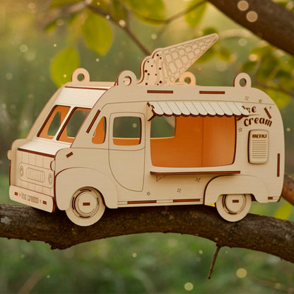 Laser cut wooden plywood Ice Cream Van Birdhouse or treat dispenser, shown lying on a green tree branch in a natural outdoor setting with warm golden hour sunlight. The model features an engraved ice cream cone on the roof, a menu sign, and wheels, showcasing the detailed DIY craft kit or ready-made whimsical gift.