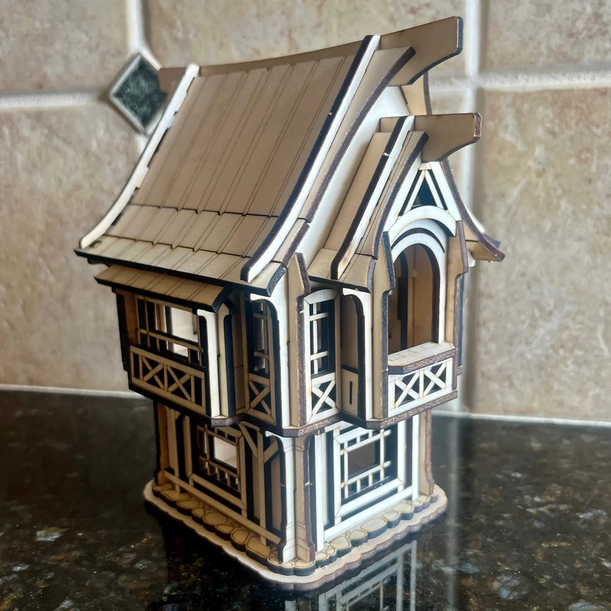 A gorgeous three-quarter view of a miniature rustic old village house with a tall brick chimney made from laser cut plywood.