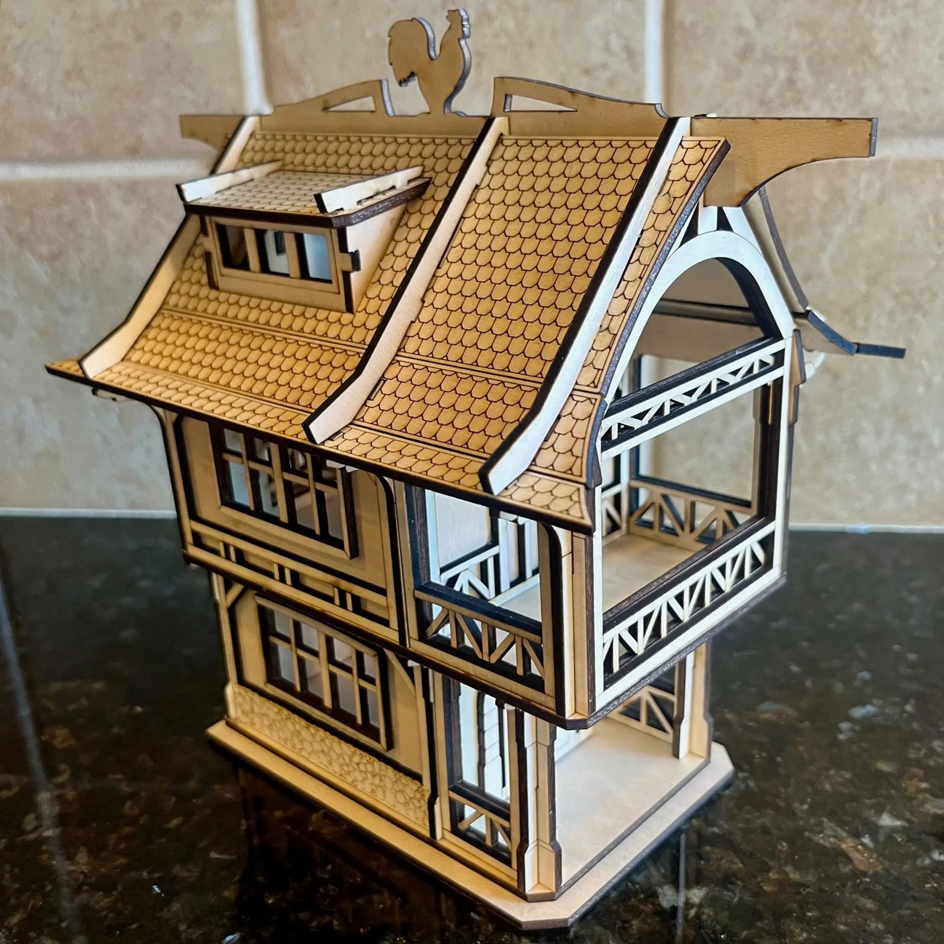 Side angle view of a medieval laser cut plywood house showing open balconies, interior floors, and a rooster weather vane.