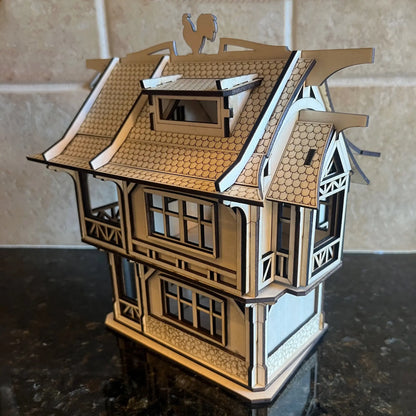 Three-quarter angle view of a medieval laser cut plywood house with a curved shingle roof and a rooster weather vane on top.