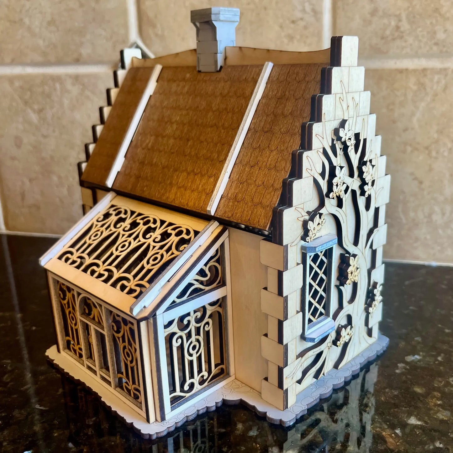 A side view of a laser cut plywood garden cottage showing an attached greenhouse conservatory with ornate filigree panels.