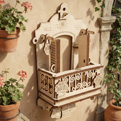 Detailed view of the laser cut plywood balcony with its hinged shutters swung open to reveal the interior space. The model shows dark burnt edges typical of laser crafting, with engraved brick patterns and hanging plant accents on either side.