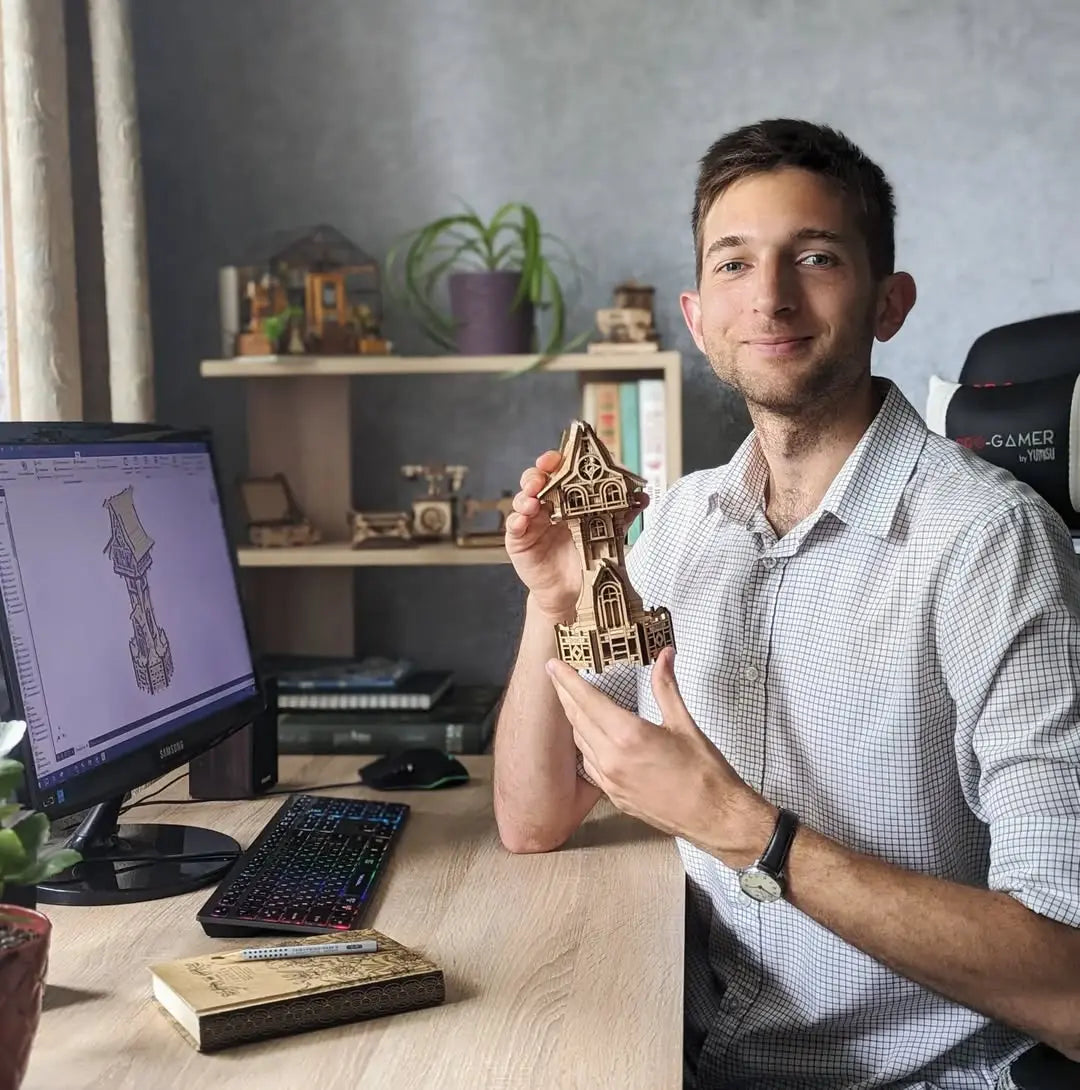 Ivan Bilous laser cut files designer holding a small model house in front of a computer screen with 3D design software.