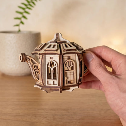 Hand holding a wooden teapot model against a blurred indoor background