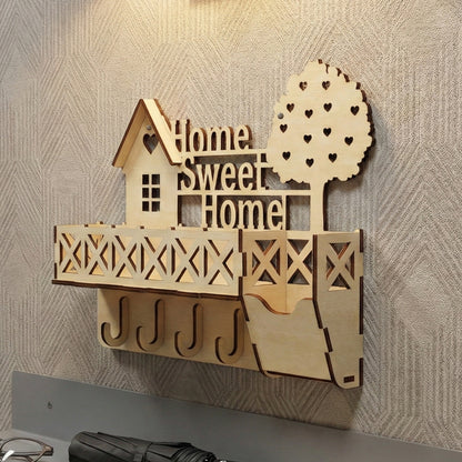 Rustic laser cut keyholder "Home Sweet Home" with layered house and tree elements, geometric balcony shelf, sturdy key hooks, and scattered heart cutouts, presented against a cozy textured wall background.