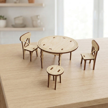 Miniature dollhouse dining set made of light-colored laser cut plywood. Features a round table with decorative grooves, two cross-back chairs, and a small round stool. The set is displayed on a wooden surface with a soft-focus kitchen background.