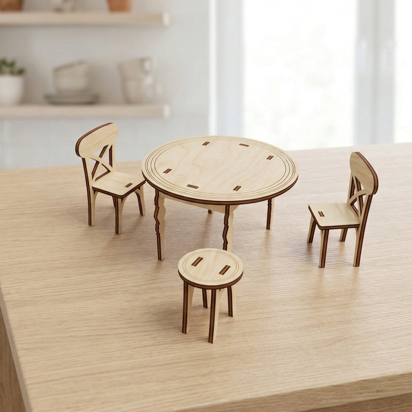 Three-piece dollhouse kitchen furniture set made of light-toned laser cut plywood. Includes a round pedestal table with etched border, two slat-back chairs with X-details, and a small round stool. Items are shown on a light wood surface to show scale.