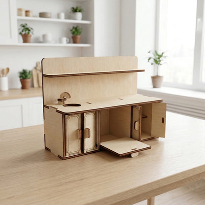 Detailed dollhouse kitchen unit crafted from laser cut plywood. Features a sink with a faucet, an upper shelf, and lower cabinets with opening doors. The light wood grain is visible, accented by dark edges and etched panel details on the doors.