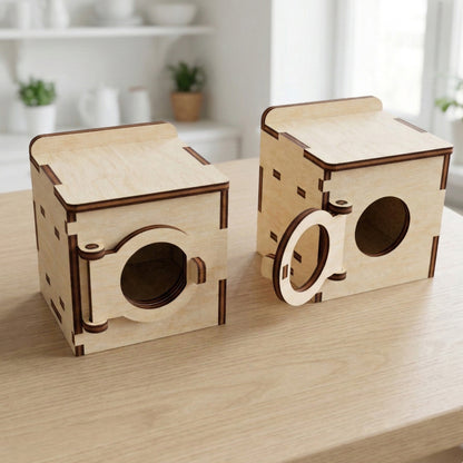 A laser cut plywood dollhouse washing machine model. It features a circular drum door with tiny engraved control panel details and knobs. The natural light wood furniture piece stands against a simple white background, showing clean edges.