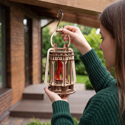 Woman hanging a handmade laser cut plywood lantern candle holder onto an outdoor metal hook in front of brick porch.