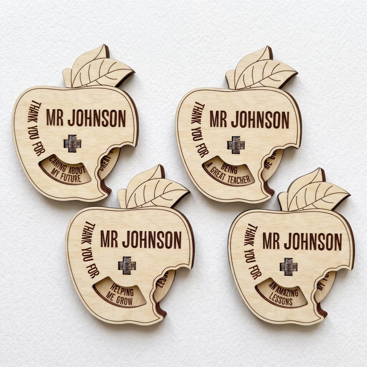 Four laser cut plywood apple teacher gifts with spinning wheel showing thank you messages laid on plain white background.