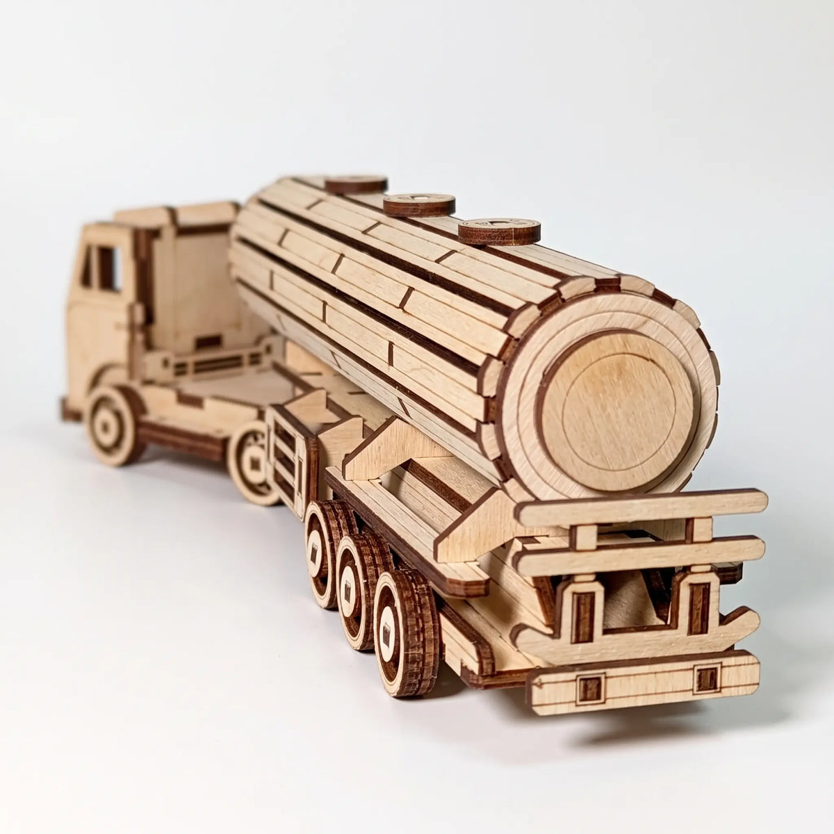 A wooden toy tanker truck model made from laser-cut plywood, shown from a three-quarters rear angle on a light gray background.