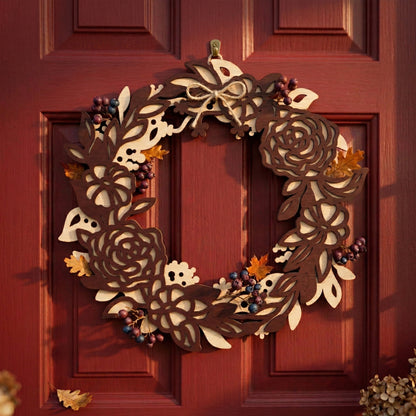 Front-facing view of a 3D layered laser-cut wooden floral wreath. The design showcases high-contrast dark and light brown plywood layers shaped into detailed roses and leaves. Mounted on a classic red door, the wreath is finished with a rustic twine bow and berry accents, perfect for autumn home decor.