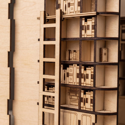 Close-up of a laser-cut birch plywood library book nook shelf featuring a tiny wooden ladder, engraved miniature books, and dark burnt edges.