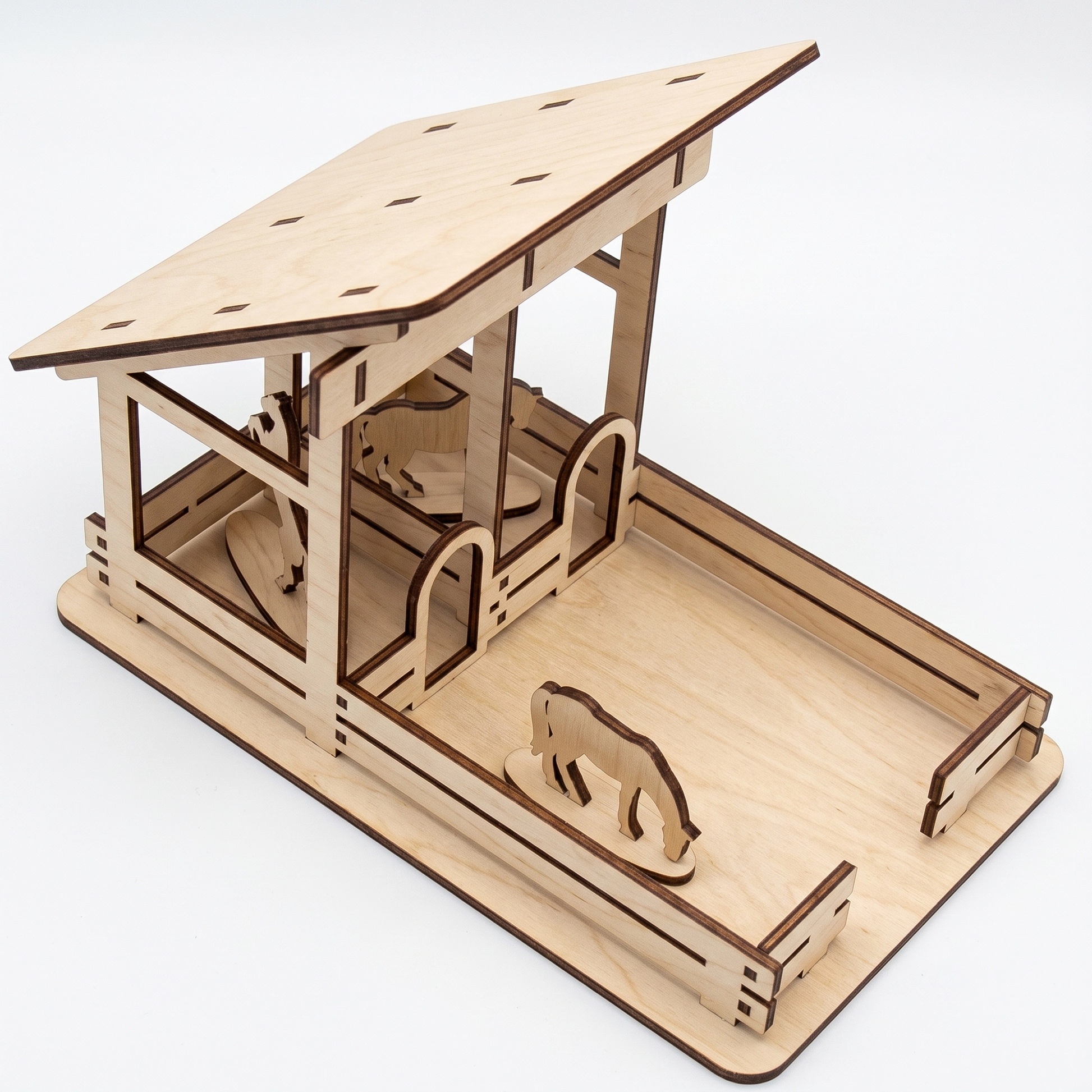 Three-quarter studio view of a laser-cut birch plywood little barn model with stalls, fencing, and horse figurines