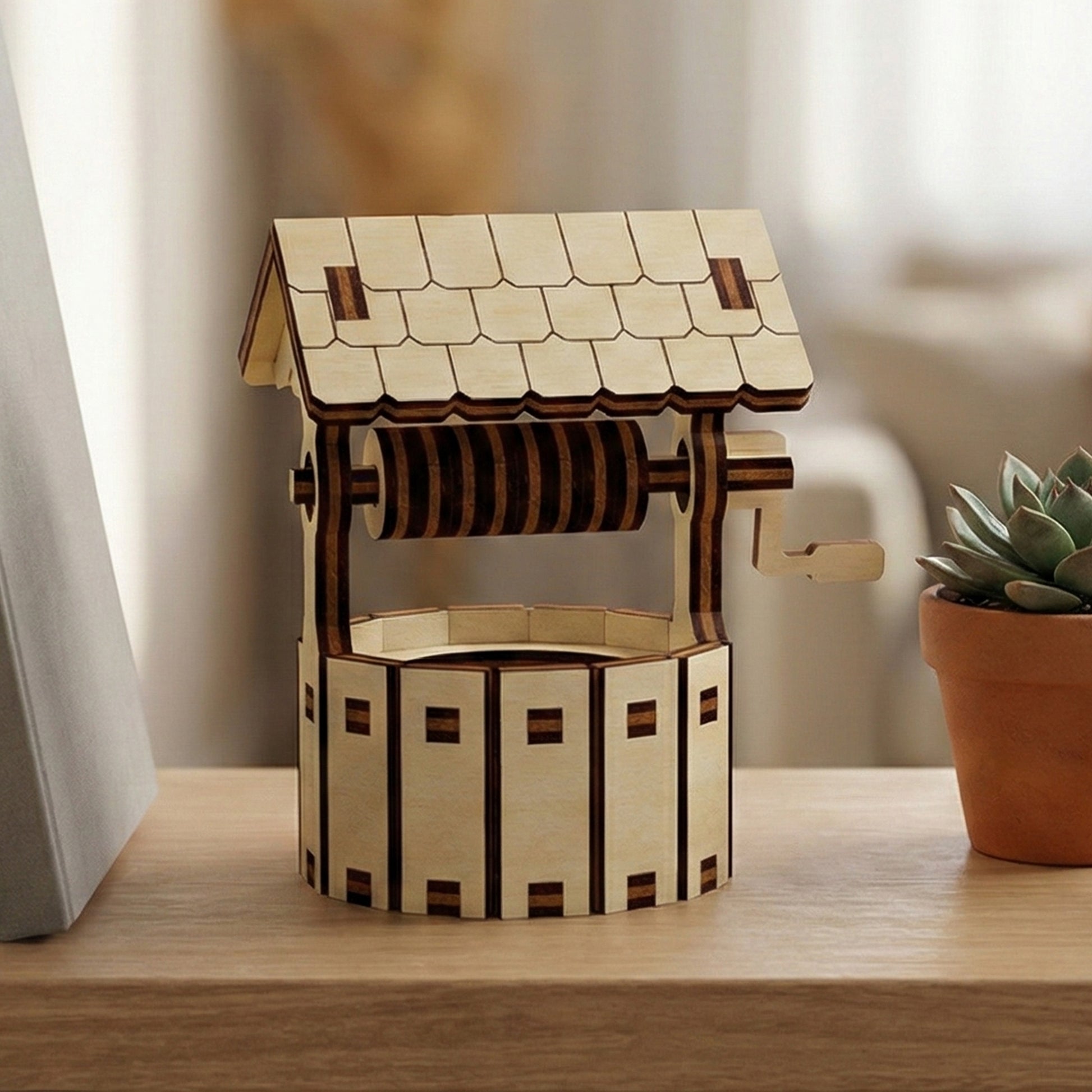 Wooden laser cut Little well model with detailed shingled roof, functional crank handle, and stone-patterned base, displayed against a softly blurred indoor background with a succulent plant.