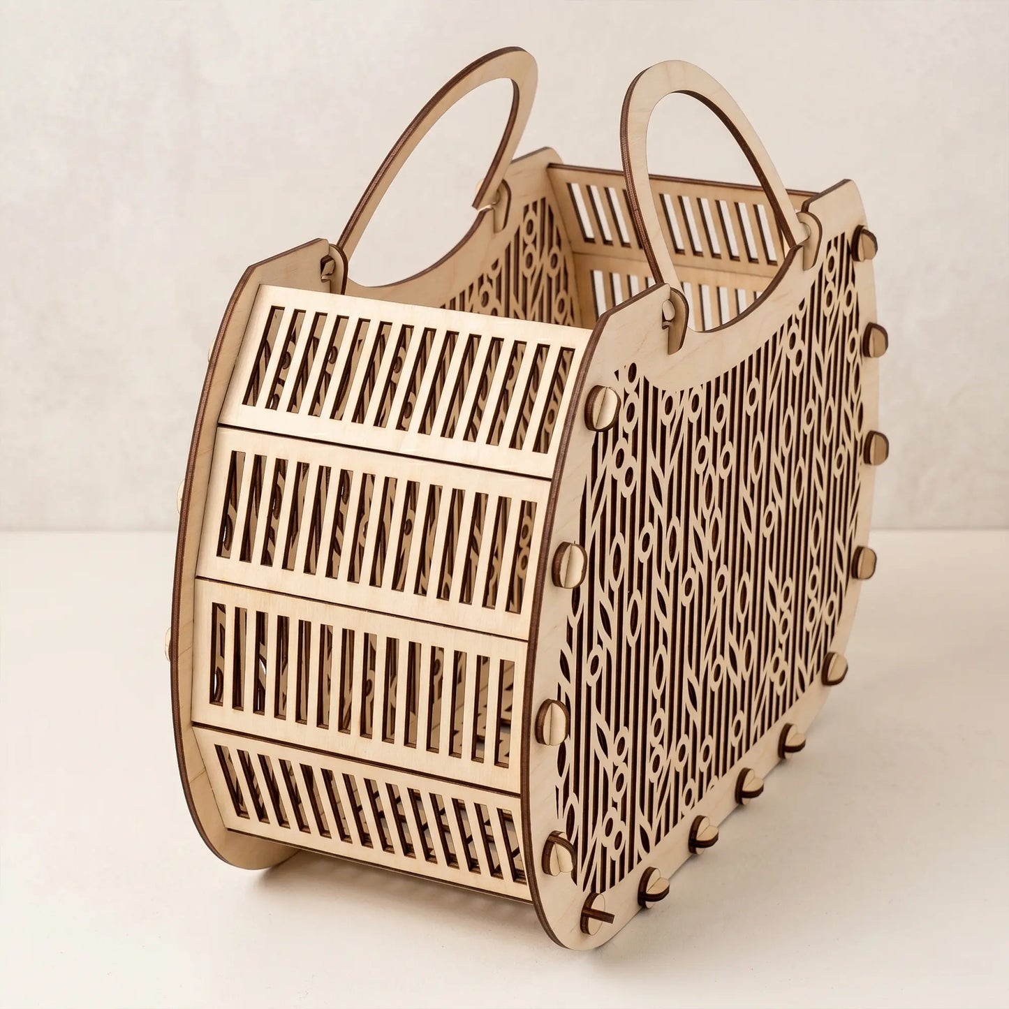 Side view of an empty laser cut plywood basket showing its flexible slatted wooden base and intricate cutout details.