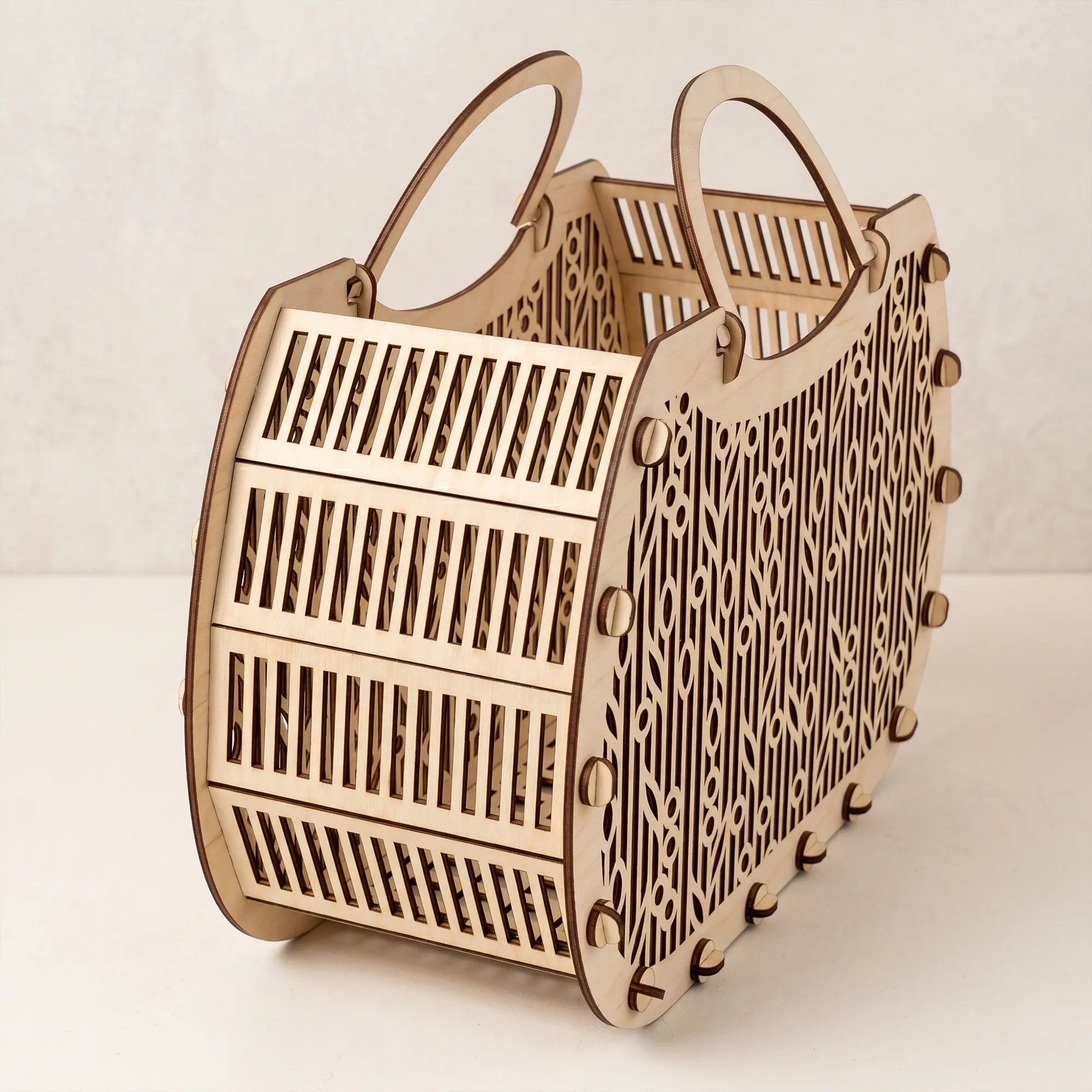 Side view of an empty laser cut plywood basket showing its flexible slatted wooden base and intricate cutout details.