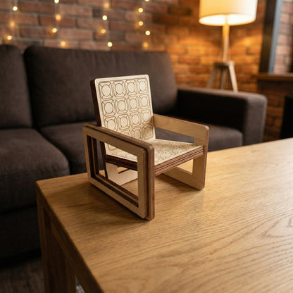 A miniature armchair made of laser cut plywood with a detailed geometric engraved pattern on the seat and backrest. The open-frame design highlights the precision of the laser cutting. Placed on a solid oak table.