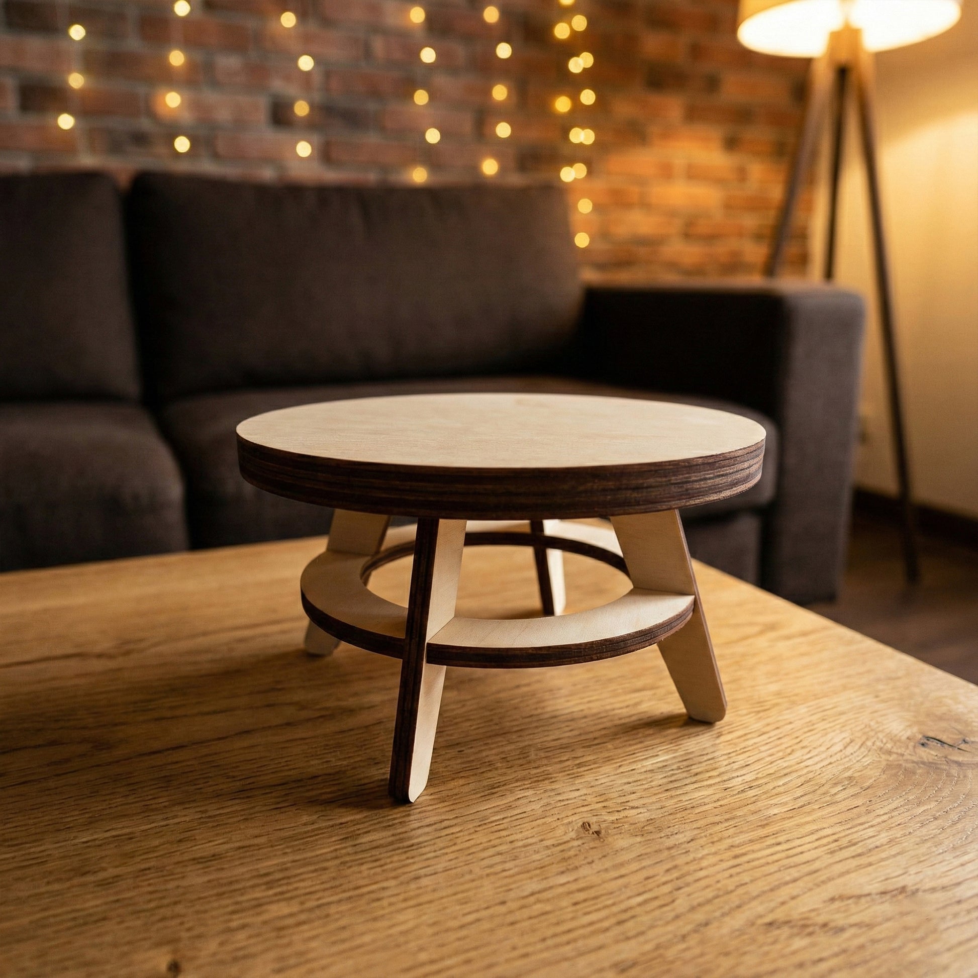 A minimalist round coffee table for dollhouses, made of laser cut plywood. Features a cross-base design with a circular support ring. The smooth birch surface and dark burnt edges emphasize the modern architectural style.