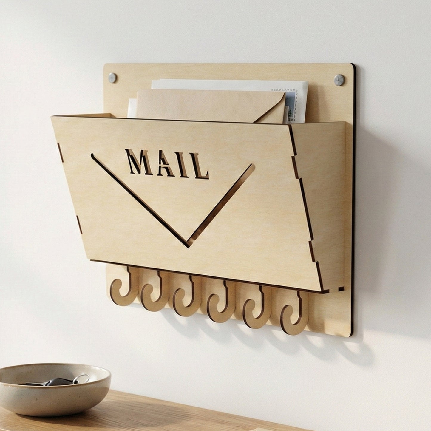 Wall-mounted laser cut plywood mail organizer with "MAIL" engraved on the front. Features six integrated J-shaped key hooks at the bottom. Shown holding several envelopes against a minimalist white wall above a wooden entryway table.