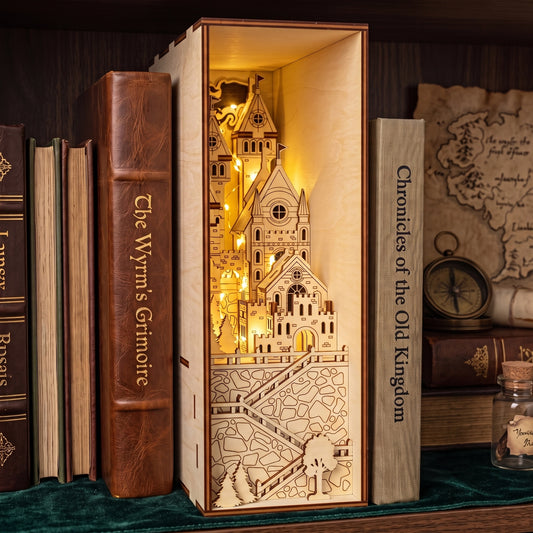 An illuminated laser cut plywood medieval castle book nook displayed on a shelf between vintage books.