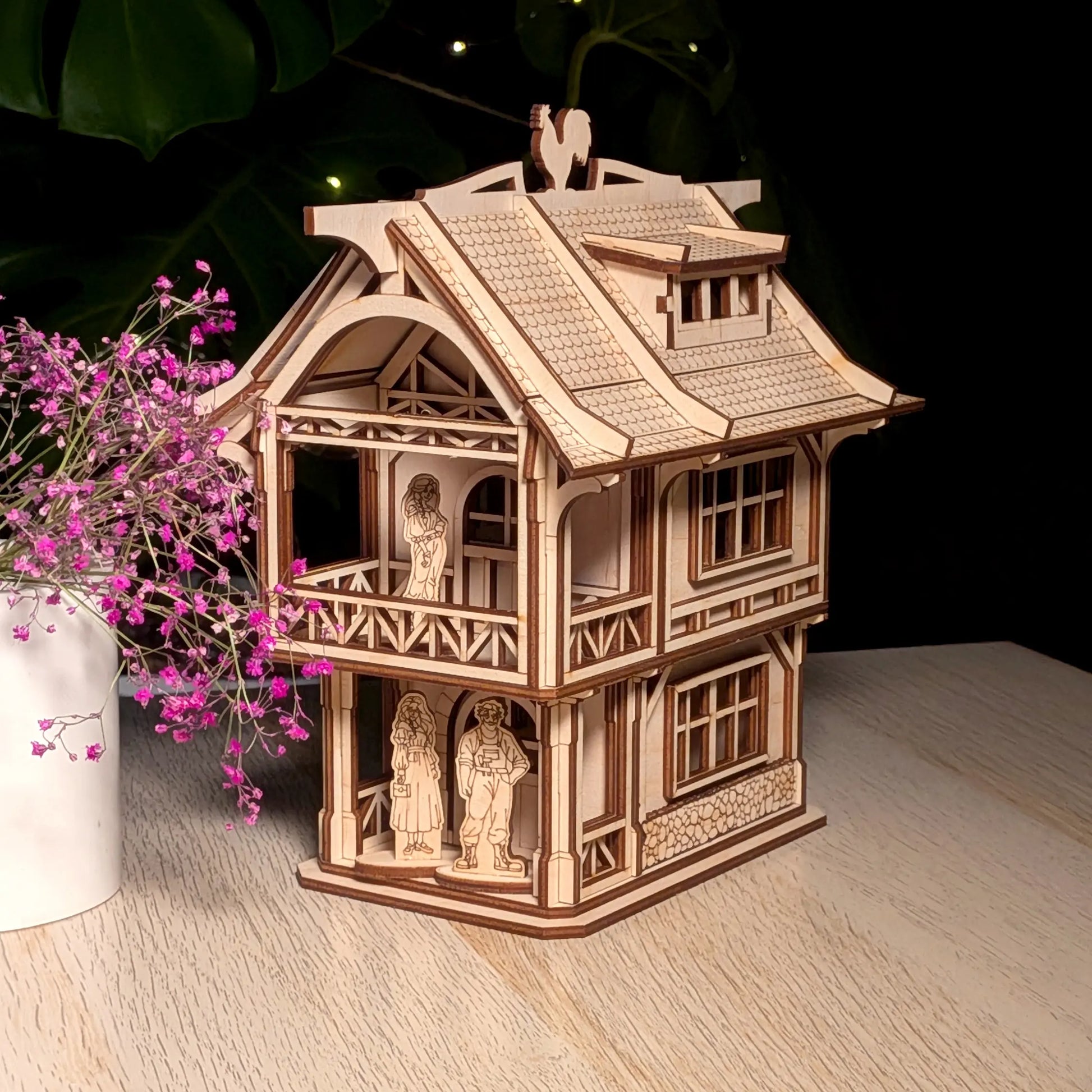 Medieval laser cut plywood townhouse model on a table next to a white ceramic vase filled with delicate purple flowers