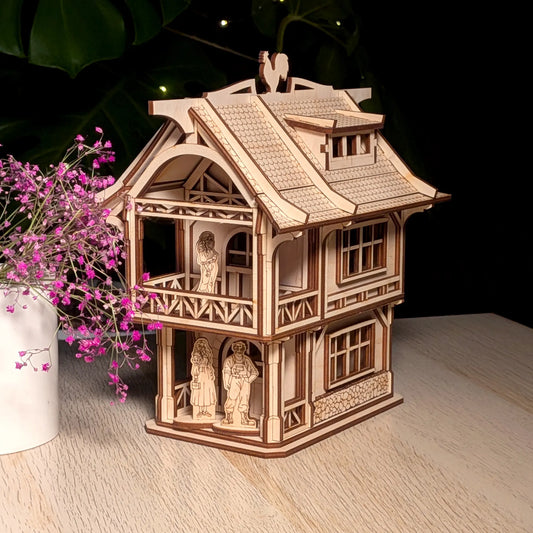 Medieval laser cut plywood townhouse model on a table next to a white ceramic vase filled with delicate purple flowers