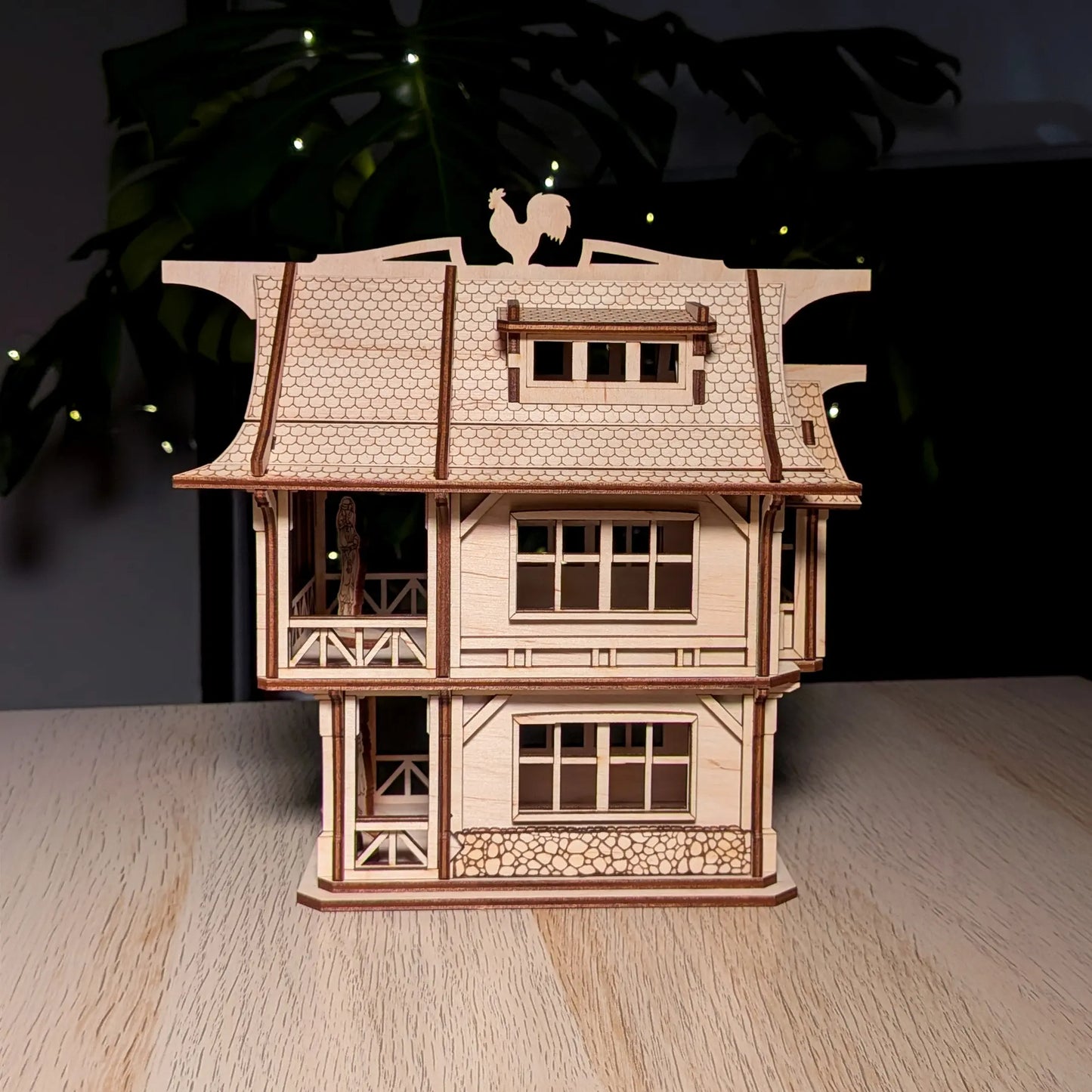 Straight front view of an intricate medieval laser cut plywood townhouse model with a rooster weather vane on a wood table.