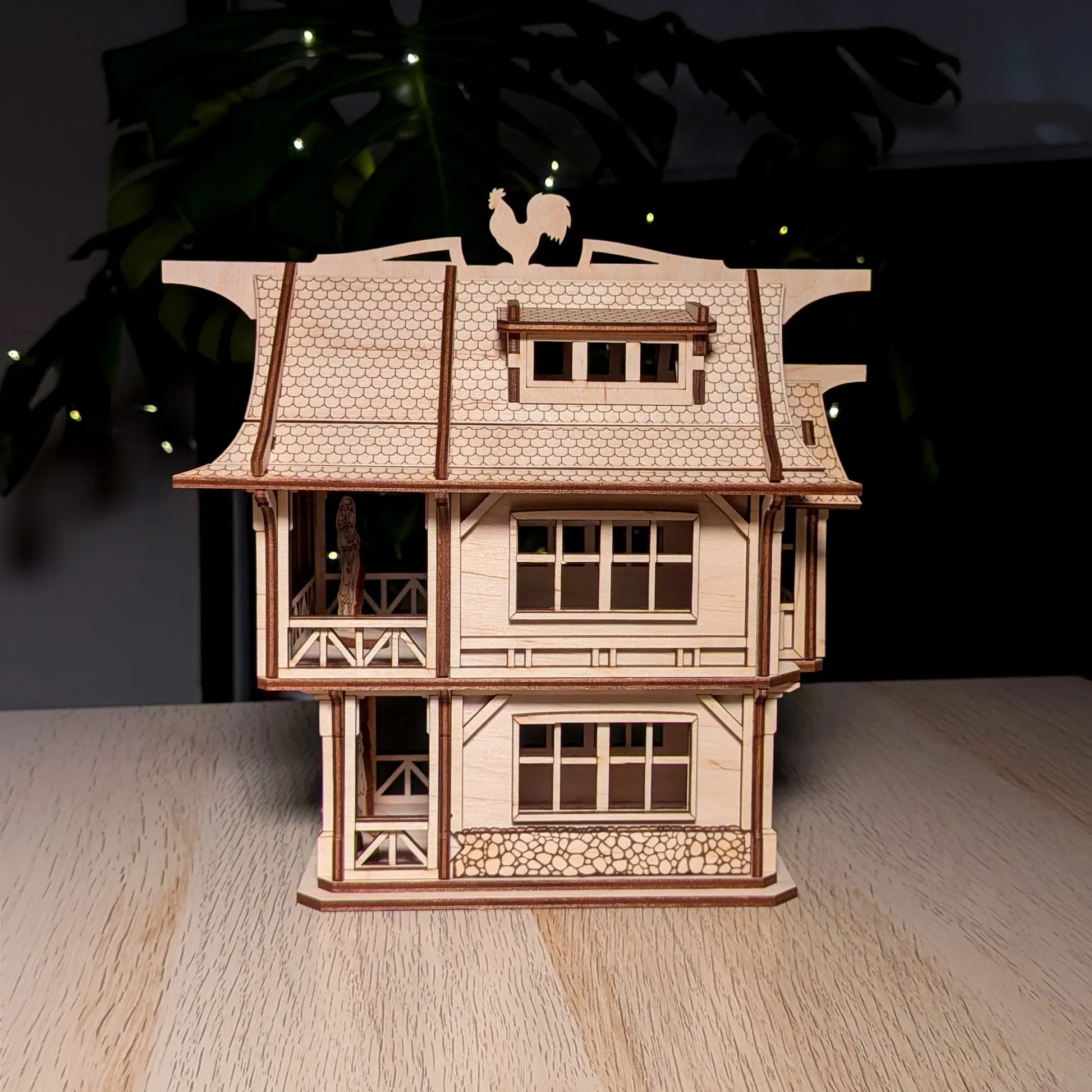 Straight front view of an intricate medieval laser cut plywood townhouse model with a rooster weather vane on a wood table.
