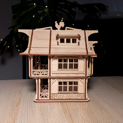 Straight front view of an intricate medieval laser cut plywood townhouse model with a rooster weather vane on a wood table.