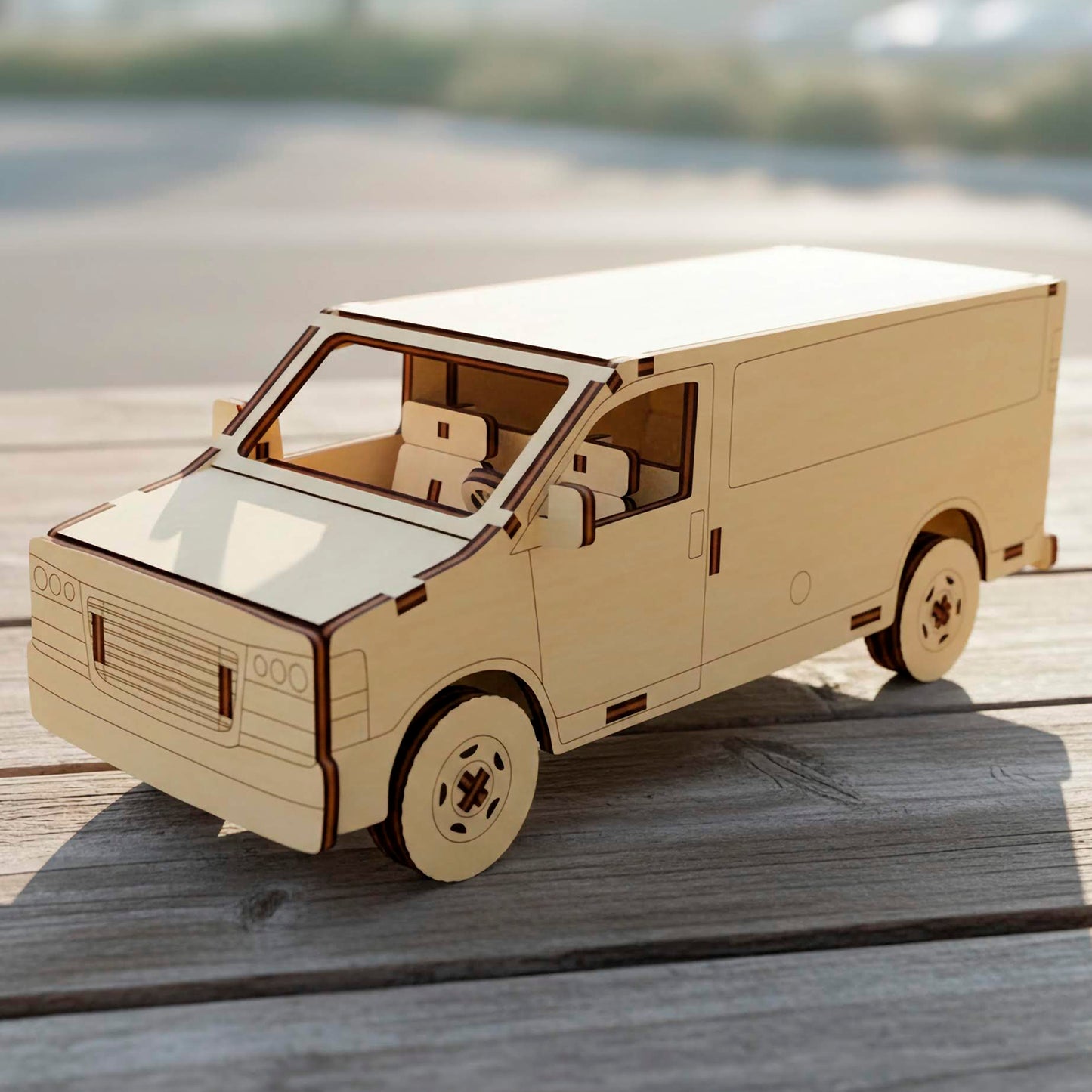 Three-quarter view of a laser cut wooden plywood  van model. Highlights intricate interior seats, a steering wheel, and engraved front grille details. This plywood craft sits on a wooden deck under bright natural sunlight.