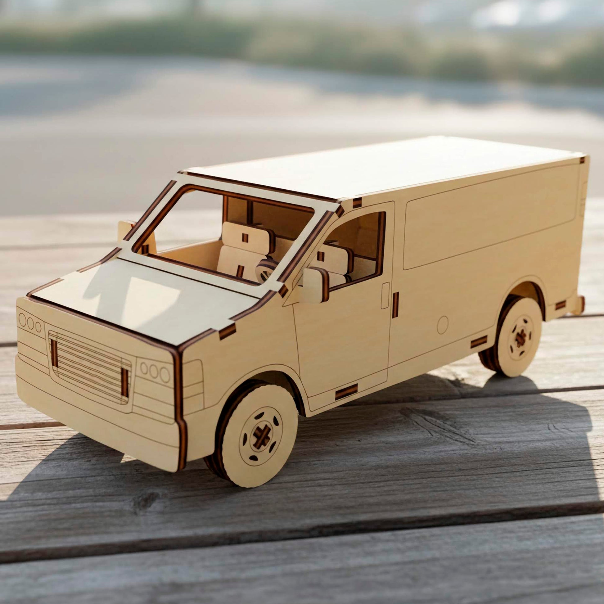 Three-quarter view of a laser cut wooden plywood  van model. Highlights intricate interior seats, a steering wheel, and engraved front grille details. This plywood craft sits on a wooden deck under bright natural sunlight.