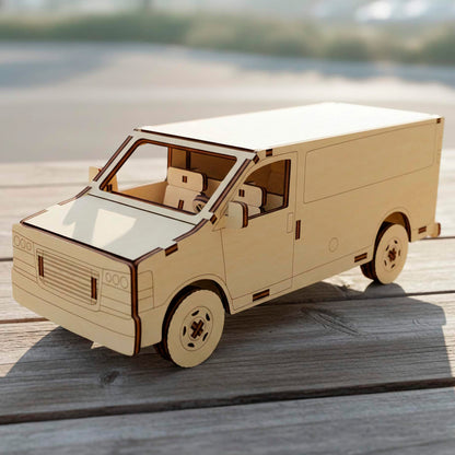 Three-quarter view of a laser cut wooden plywood  van model. Highlights intricate interior seats, a steering wheel, and engraved front grille details. This plywood craft sits on a wooden deck under bright natural sunlight.
