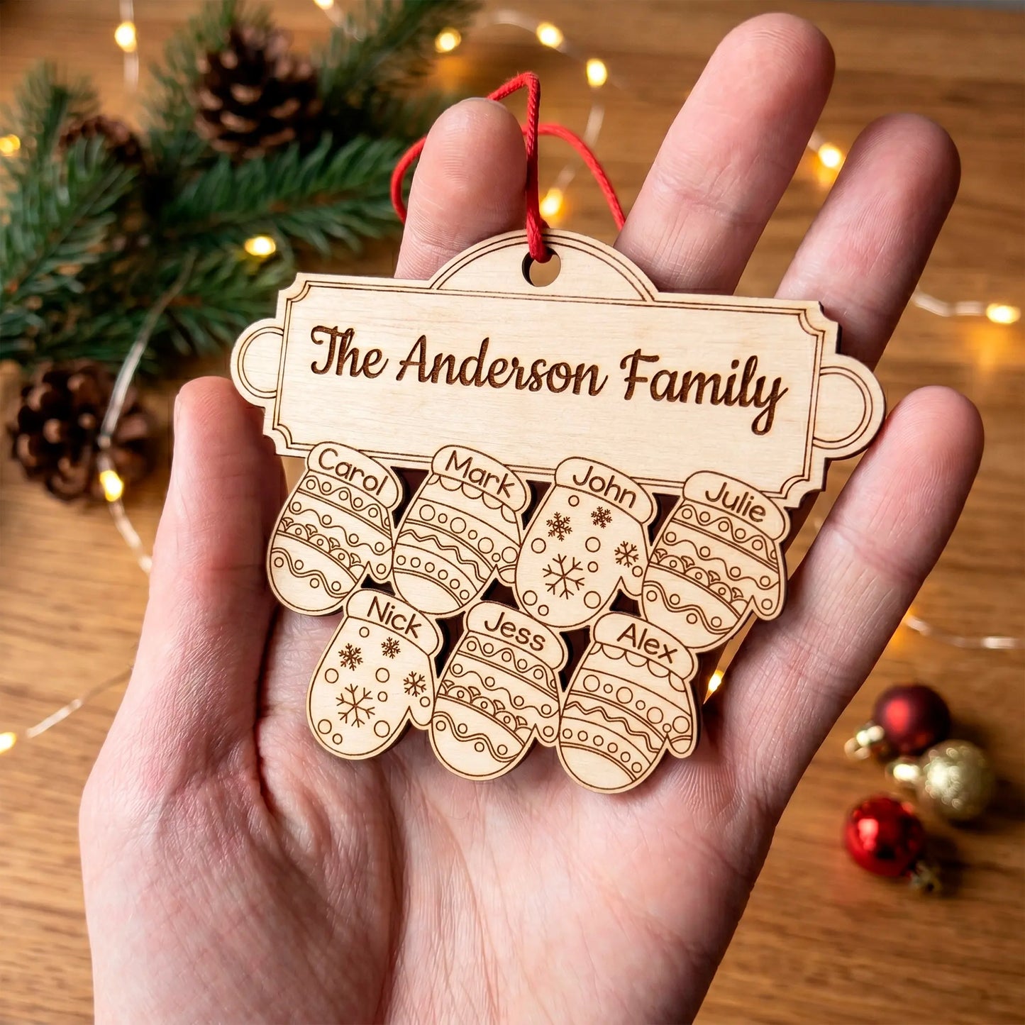 Close up of a laser cut plywood family ornament in a hand, showing 7 engraved mittens under "The Anderson Family" sign.