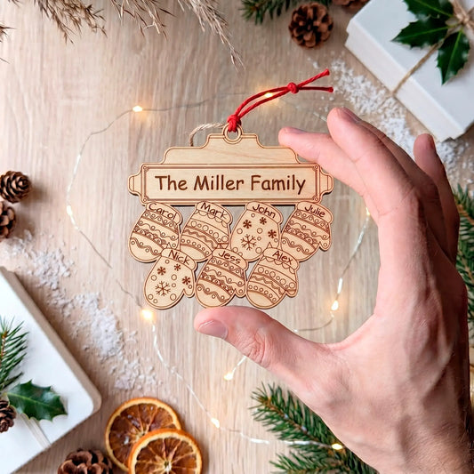 A hand holds an unpainted laser cut plywood ornament with 7 engraved, named mittens below "The Miller Family" plaque.