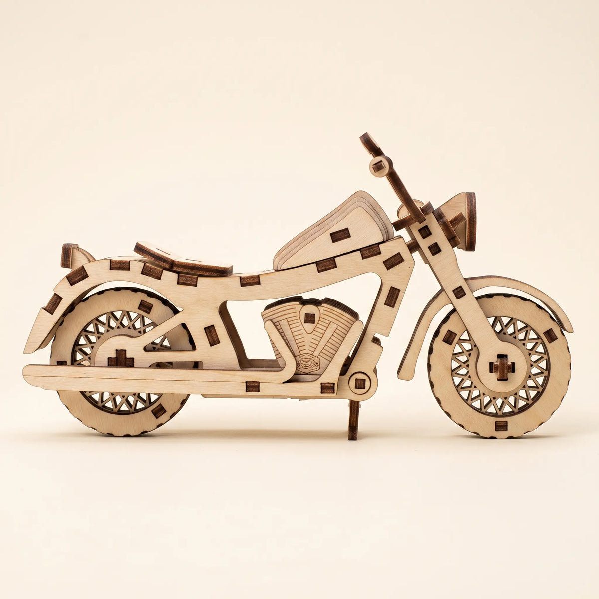 A wooden laser-cut model of motorcycle, constructed from light-colored plywood with darker brown laser-burned edges, displayed on a clean, solid cream background.
