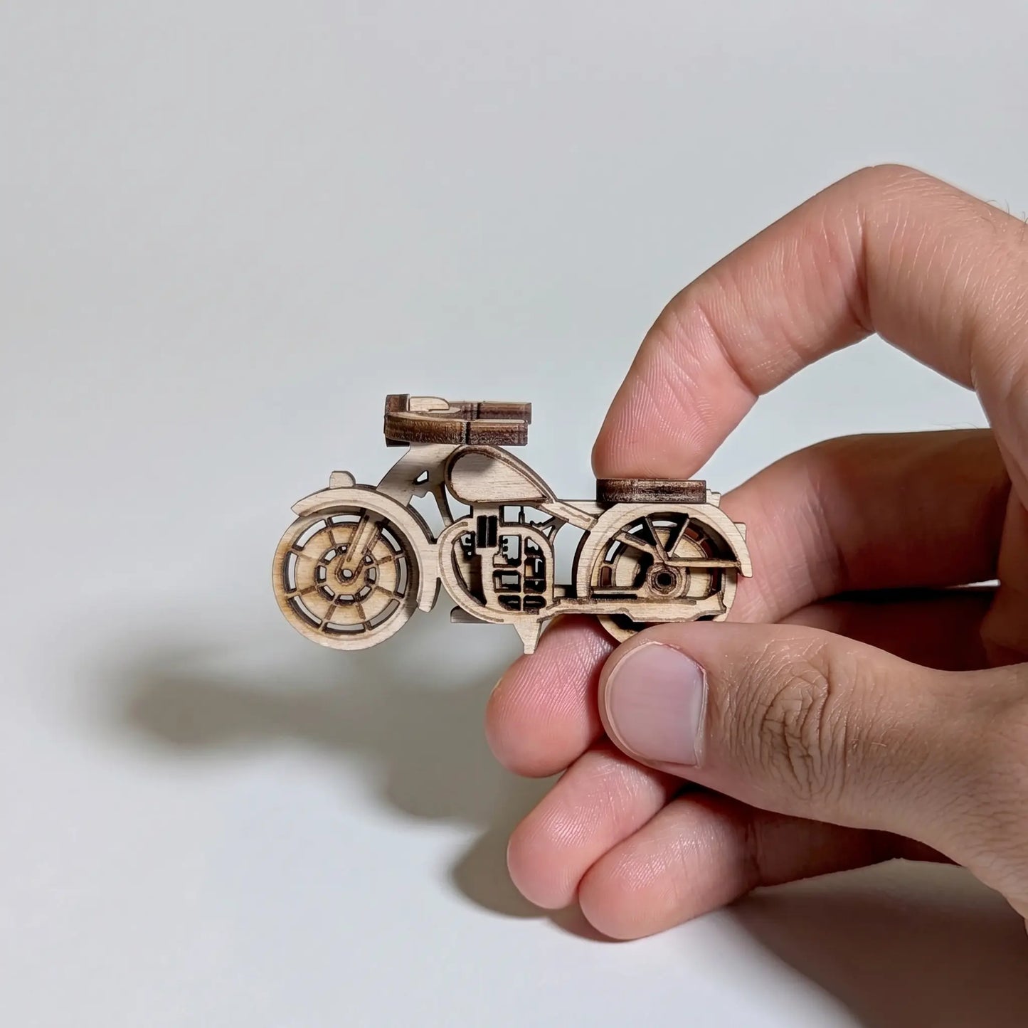 Hand holding a small wooden motorcycle model against a plain background
