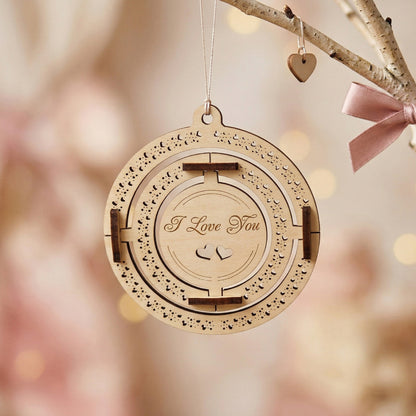 A frontal view of a 3D kinetic Valentine's Day ornament made of laser-cut plywood. The central circle is engraved with "I Love You" in elegant script, surrounded by two moving rings featuring intricate heart-shaped patterns. Handcrafted wooden gift hanging in a soft, romantic setting.